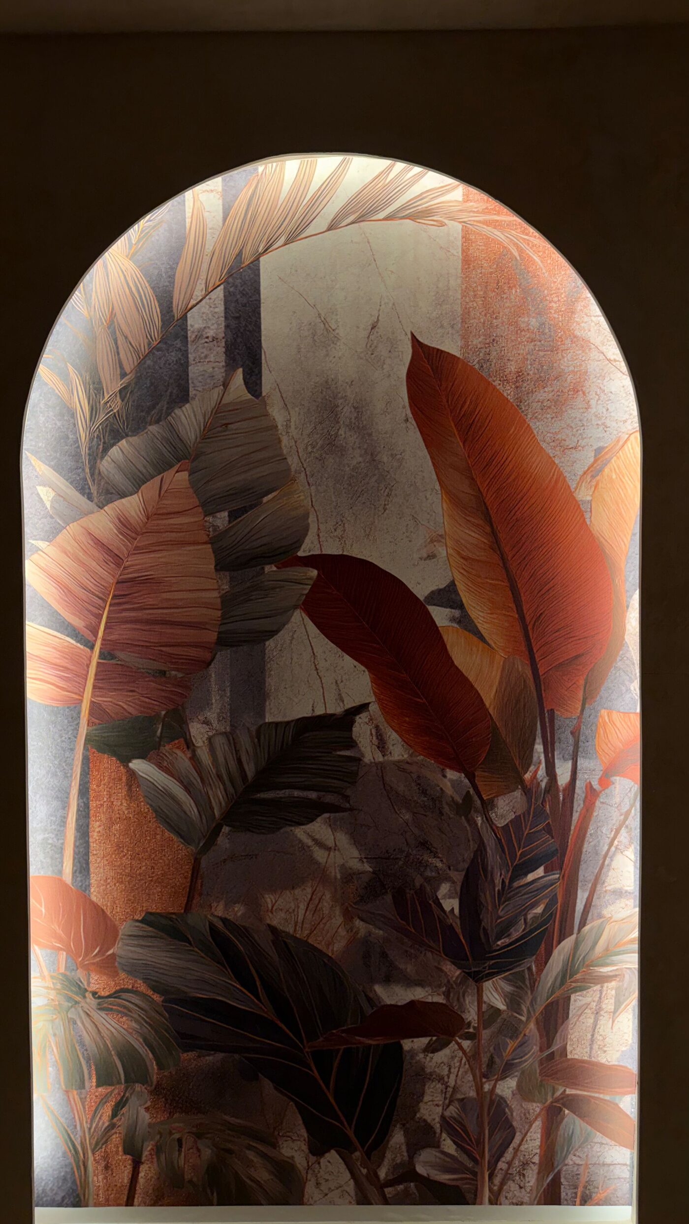 Backlit arched niche with a botanical mural of large leaves in terracotta and grey tones.