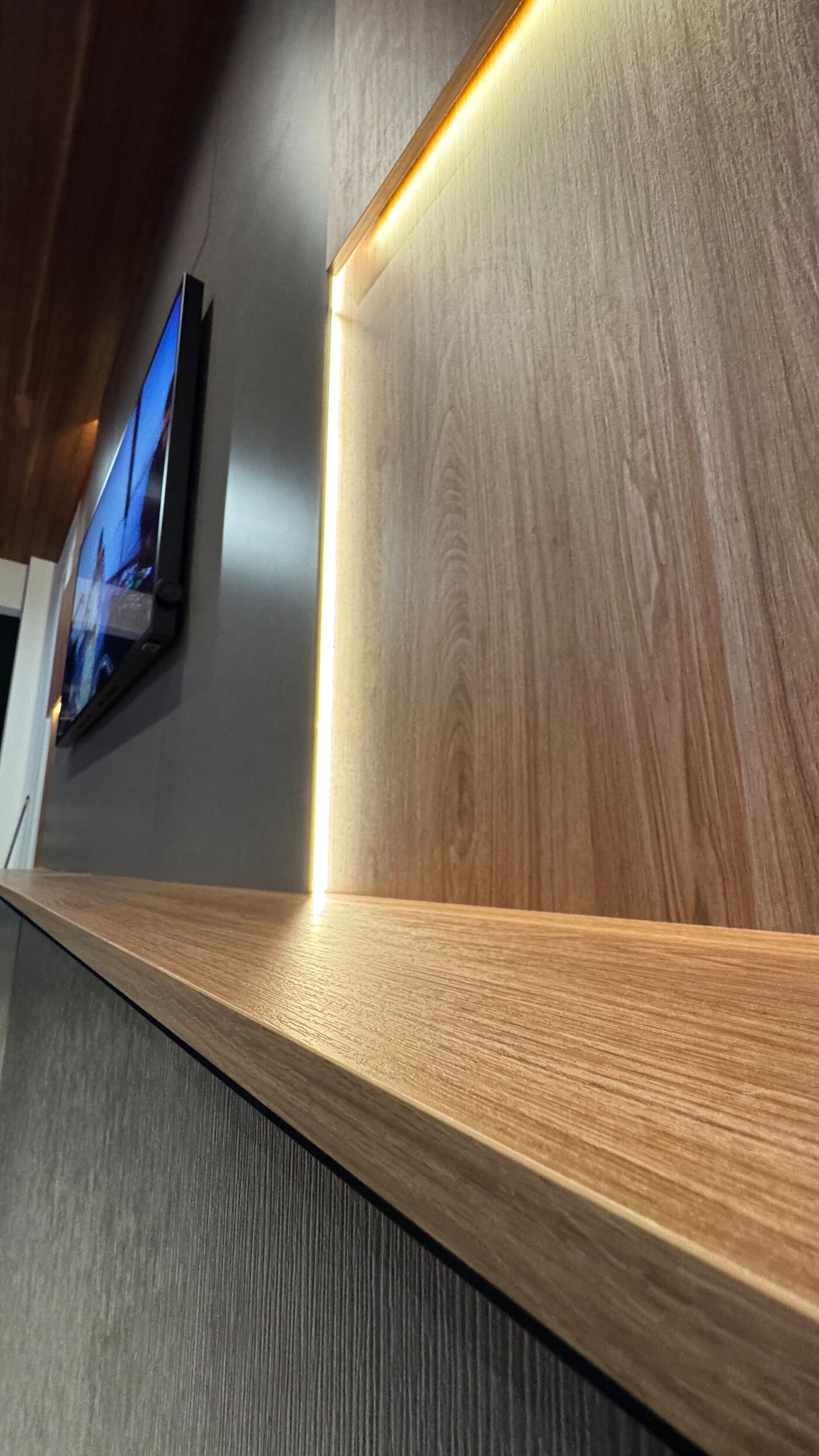 Close-up of the wood-textured panel and floating shelf lit by a vertical line of warm light.
