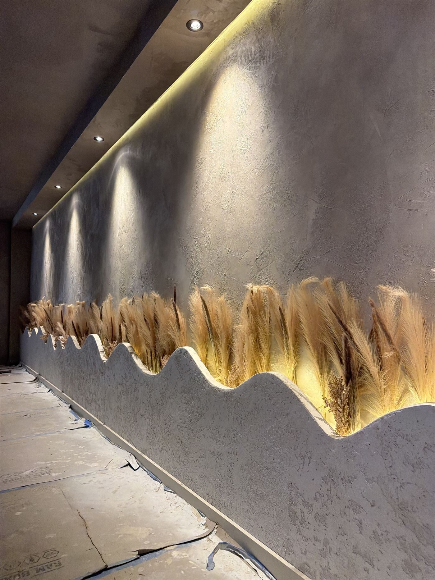 Detail: textured wall with a wavy planter of dried pampas grass under warm light.