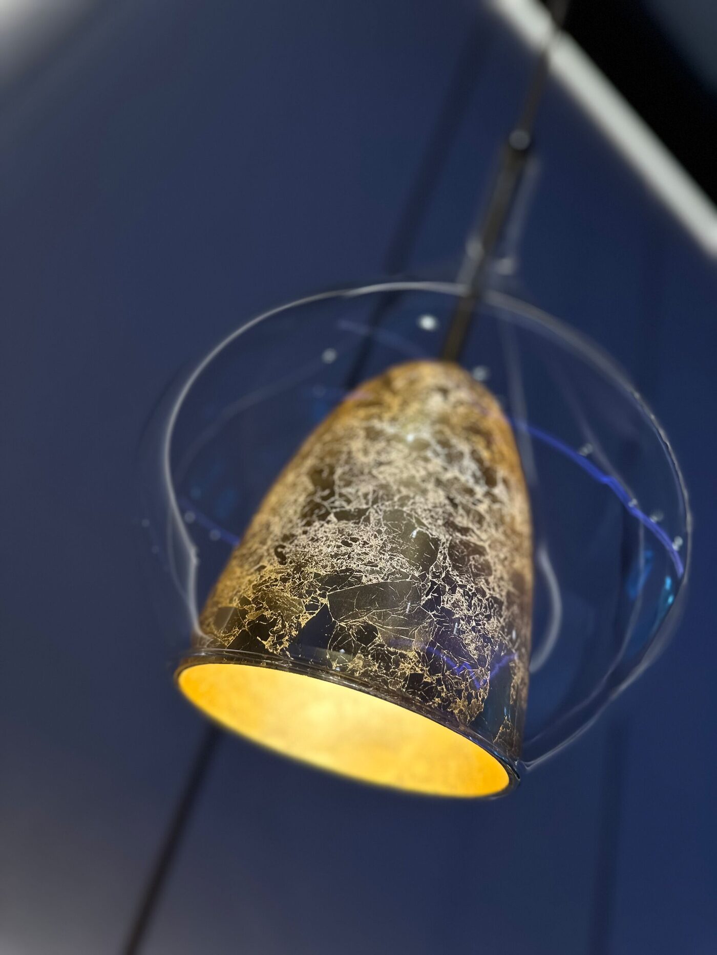 Detail: pendant lamp with a golden crackled shade inside a clear glass sphere.