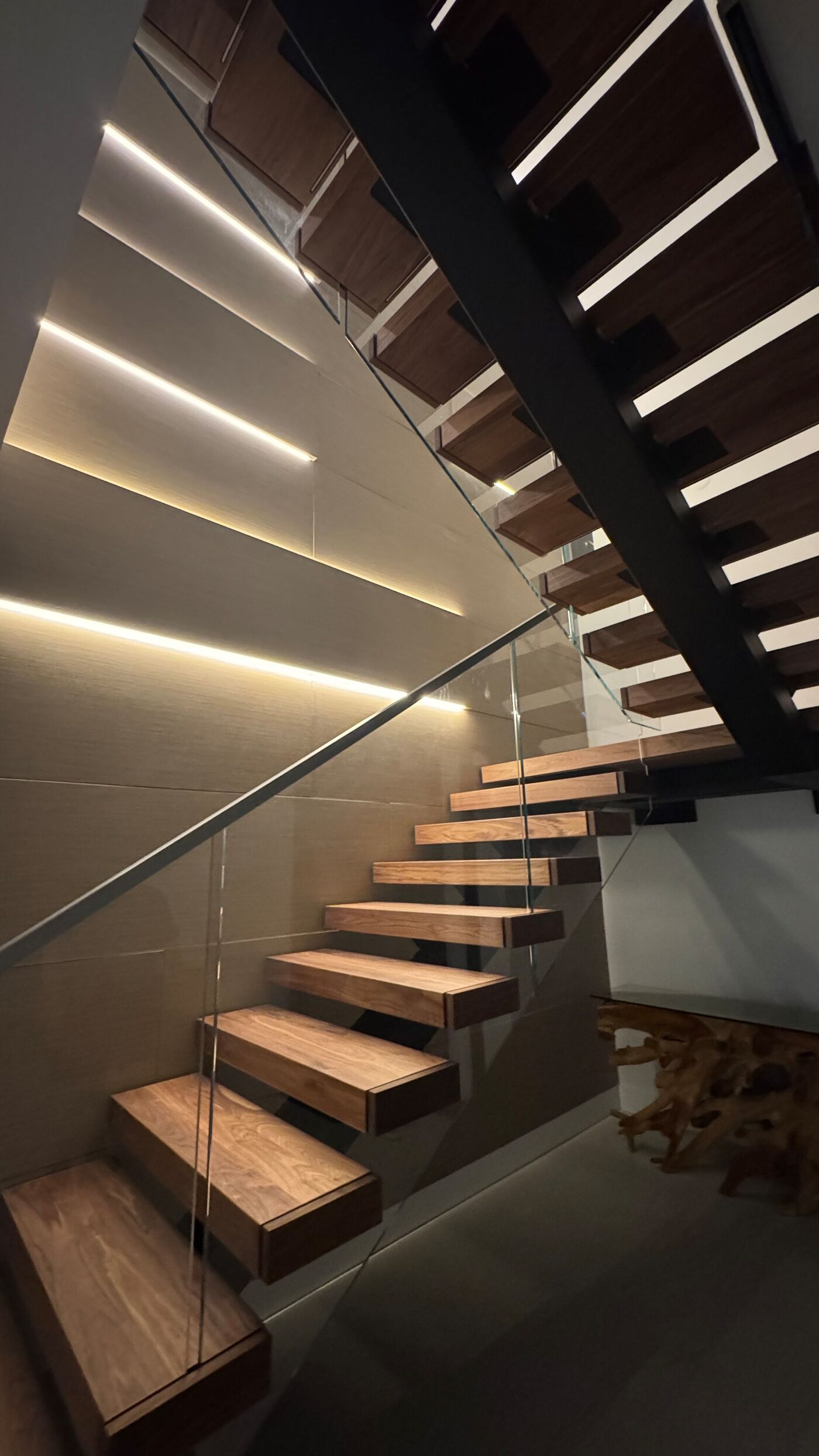 Detail: staircase beside a wall of layered wood-effect panels crossed by diagonal lines of indirect light.