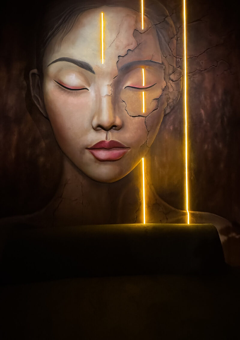 Face in relief with a cracked surface and closed eyes, crossed by vertical lines of warm LED light.